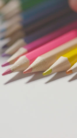 Vertical-Video-Studio-Shot-Of-Multi-Coloured-Pencils-In-A-Line-On-White-Background-With-Hand-Choosing-